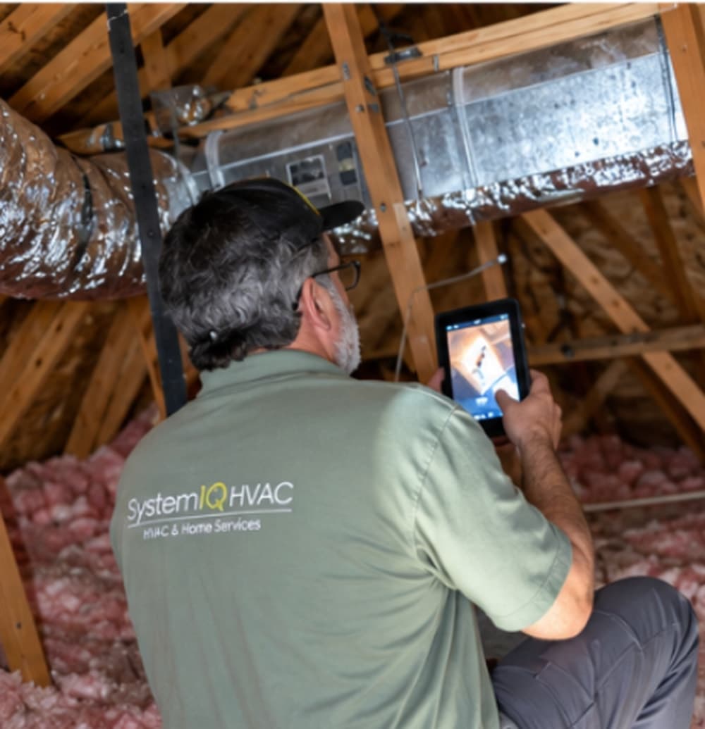 Inspecting exposed supply trunk and flex duct runs, with notes on a tablet