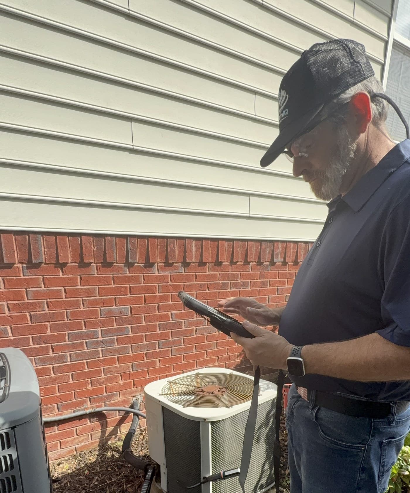Russell recording diagnostic readings on a tablet at a customer's outdoor unit during a service call